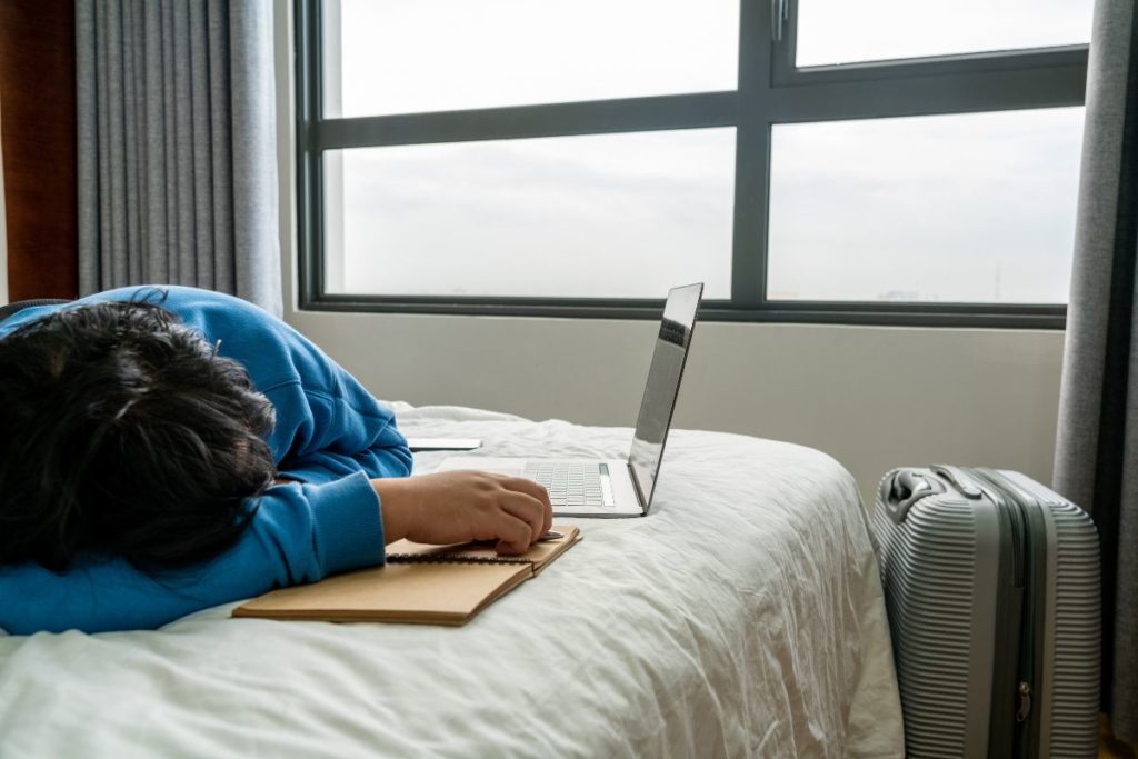 Mann schläft auf Hotelbett neben Laptop